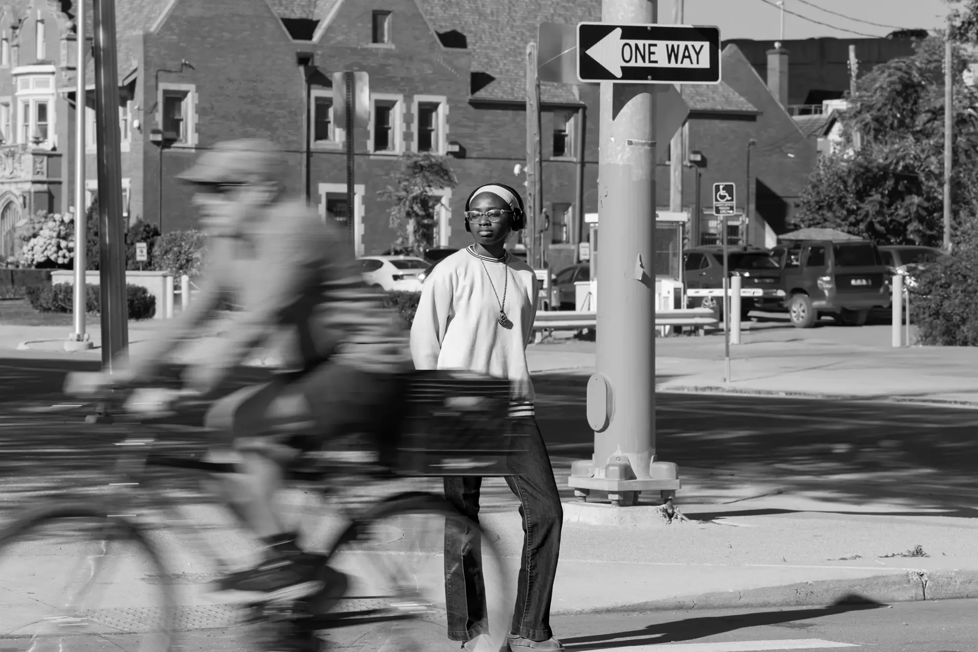 Street style fashion photography of a young woman crossing the street as someone passes on a bike—demonstrates fashion photography and a shutter speed trick.