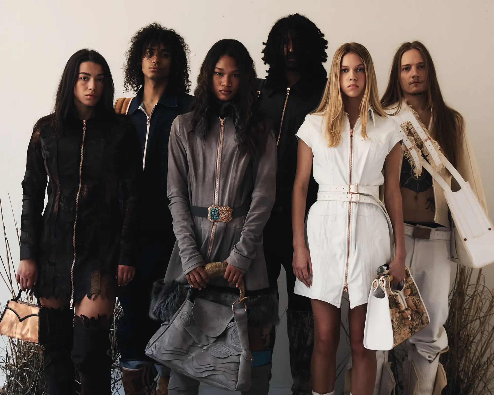 Group of models wearing leather and woven textile clothing and carrying handbags and messenger bags