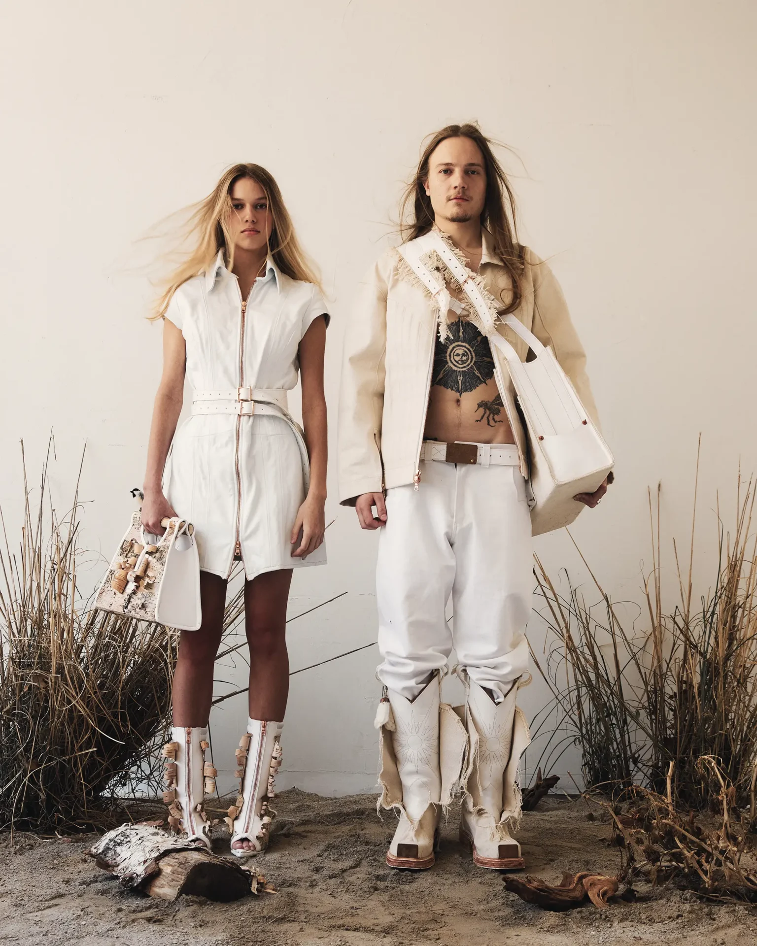 Two models wearing white clothing and boots and bags made of leather, woven textiles and birch bark
