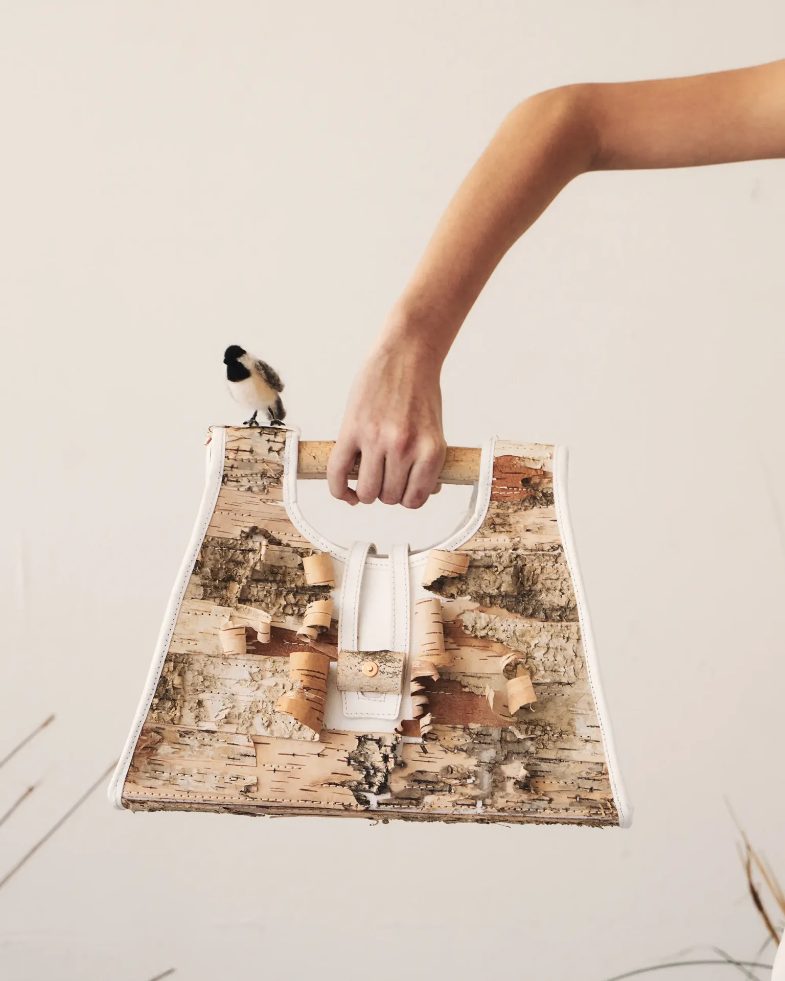 Hand holding bag made of leather and birch bark with small felt bird on handle