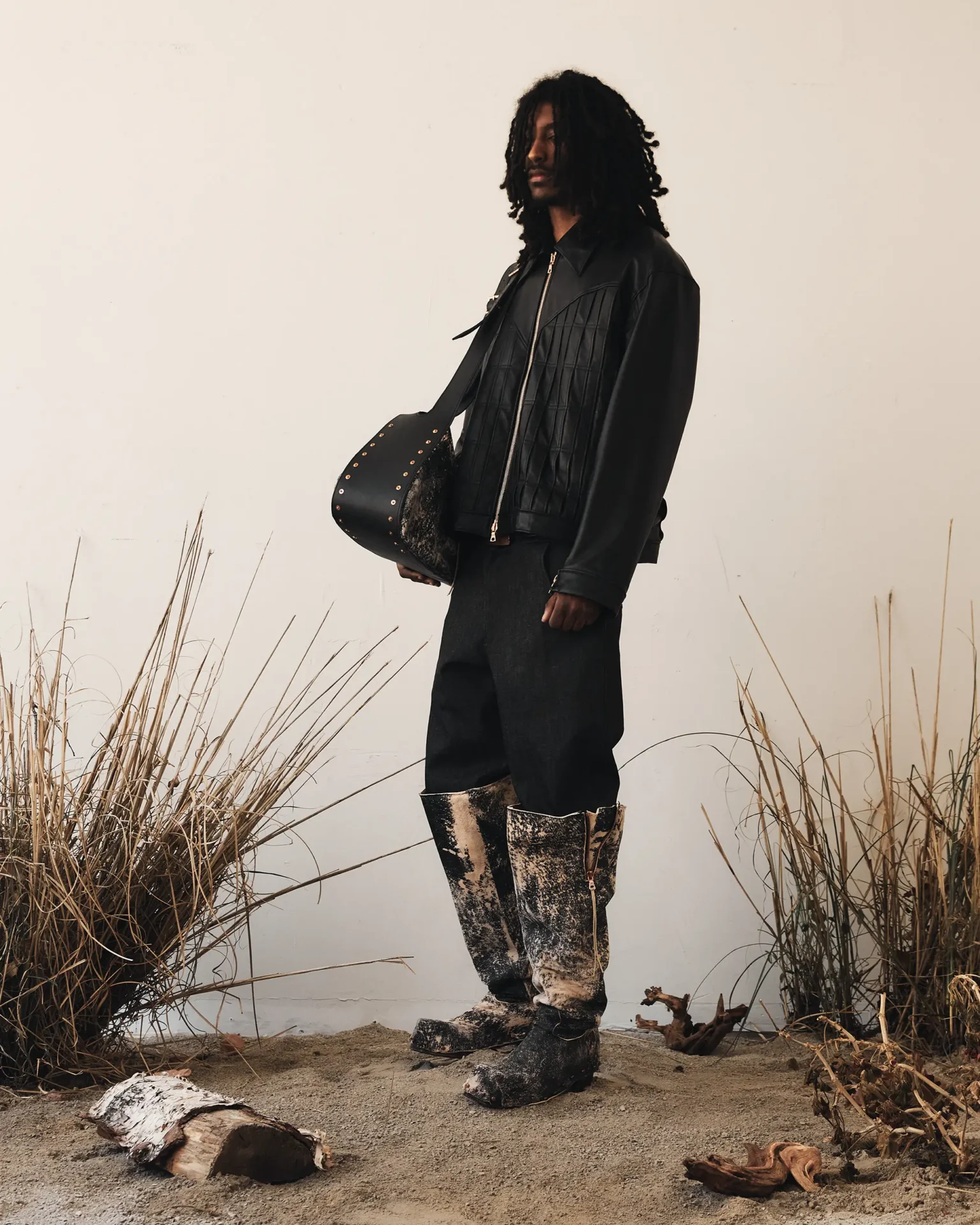 Model wearing leather knee high boots and carrying large leather bag