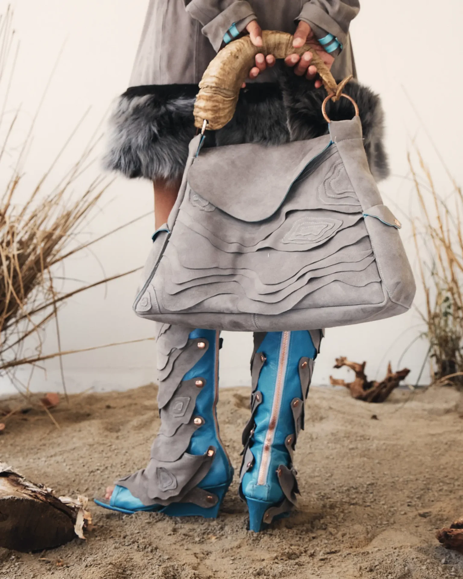 Model wearing leather knee high boots and carrying large leather bag with horn handle