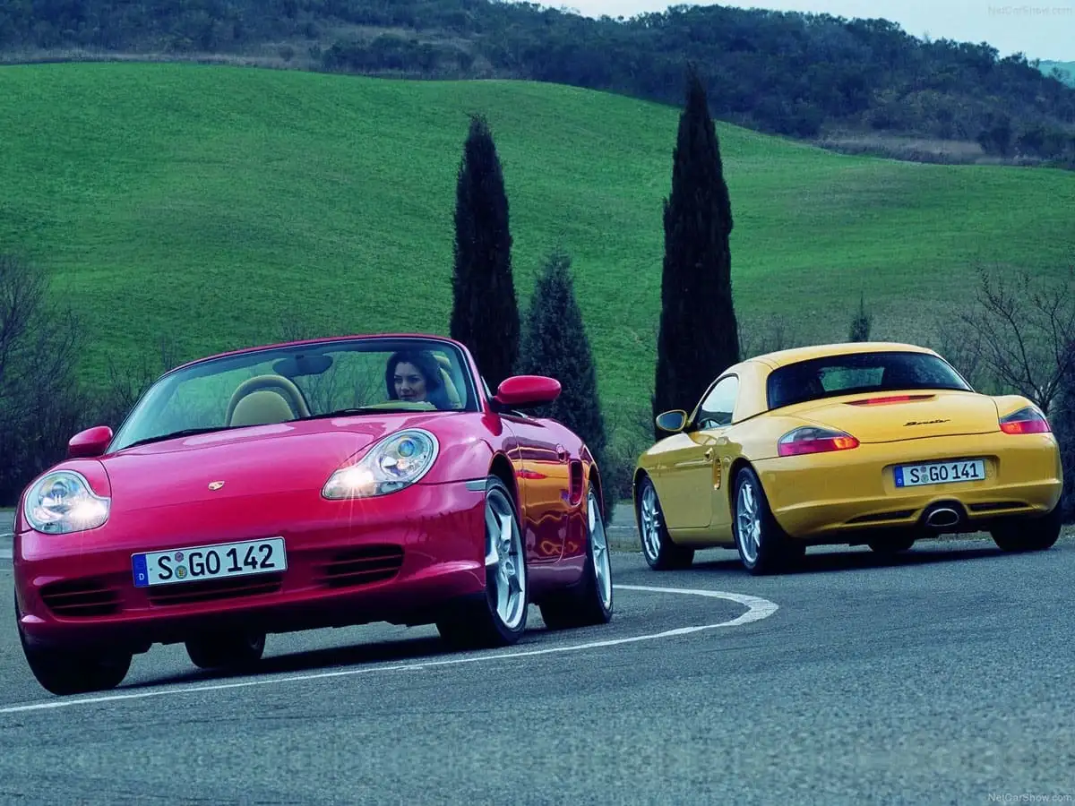 Red and yellow Porsche driving among green hills.