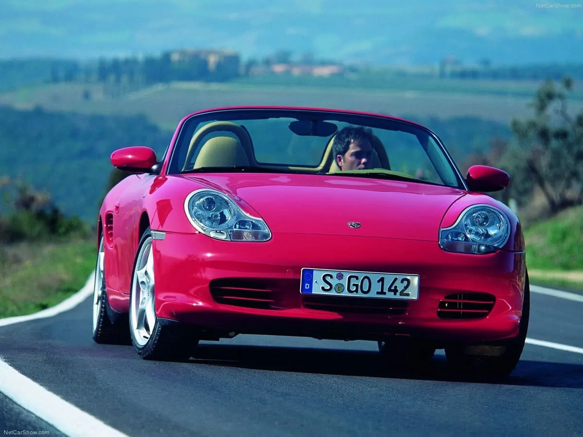 A red Porsche driving on a road in the countryside.