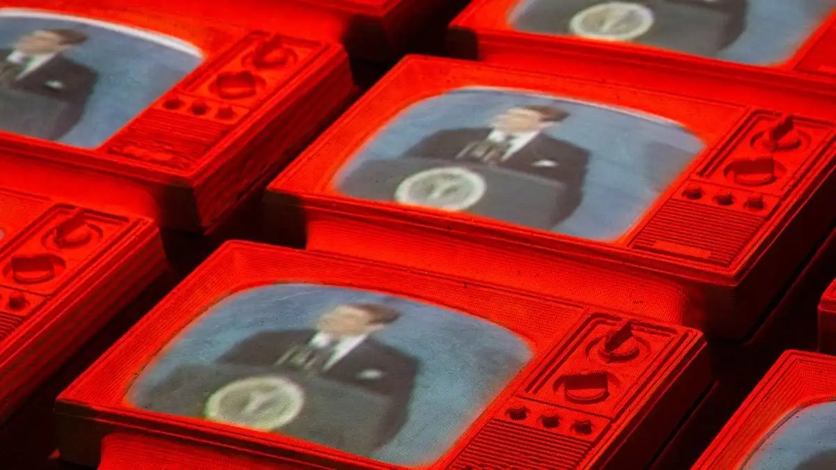 Compressed red televisions featuring a man in a suit at a podium