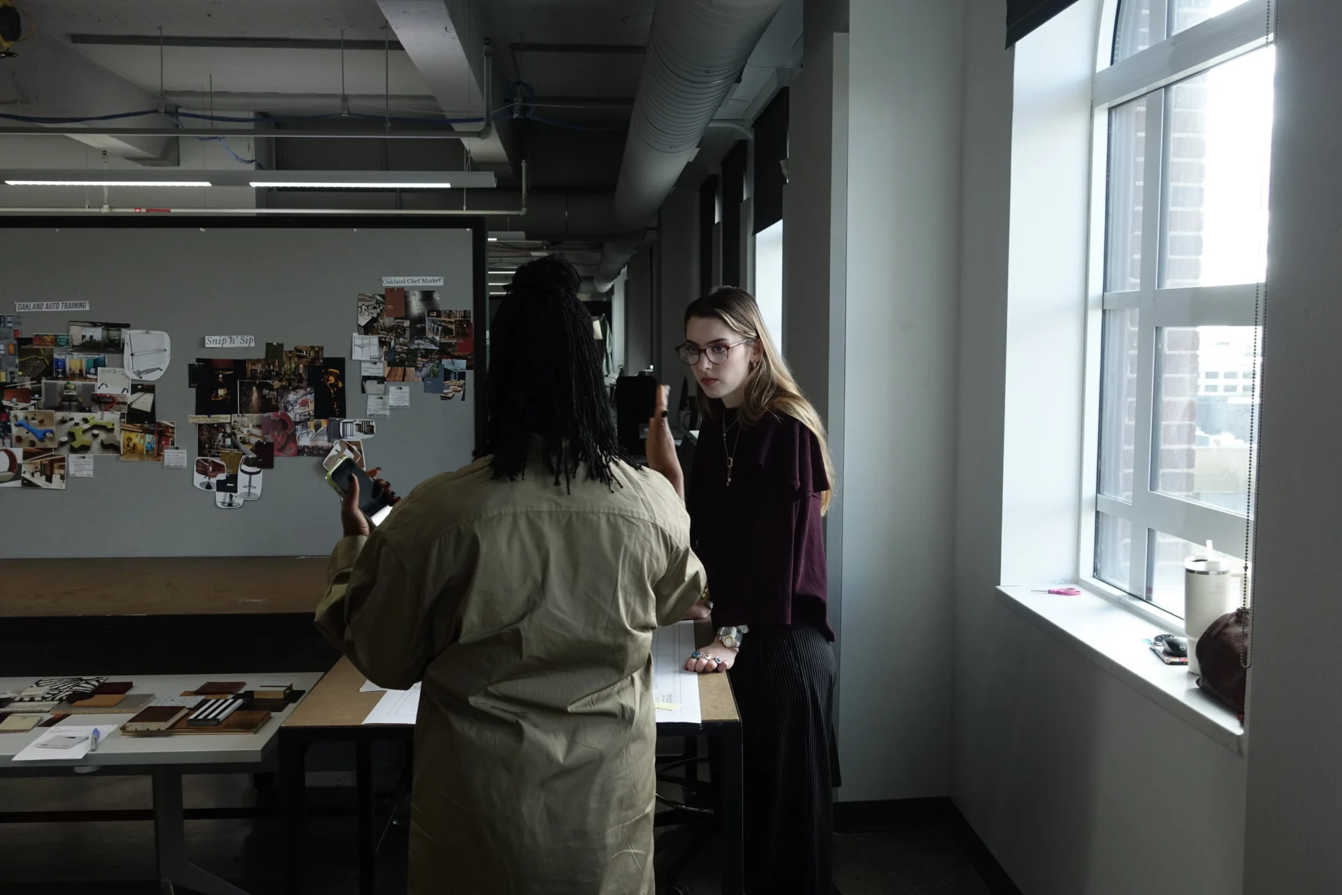 Two people having a discussion next to design research pinned to wall