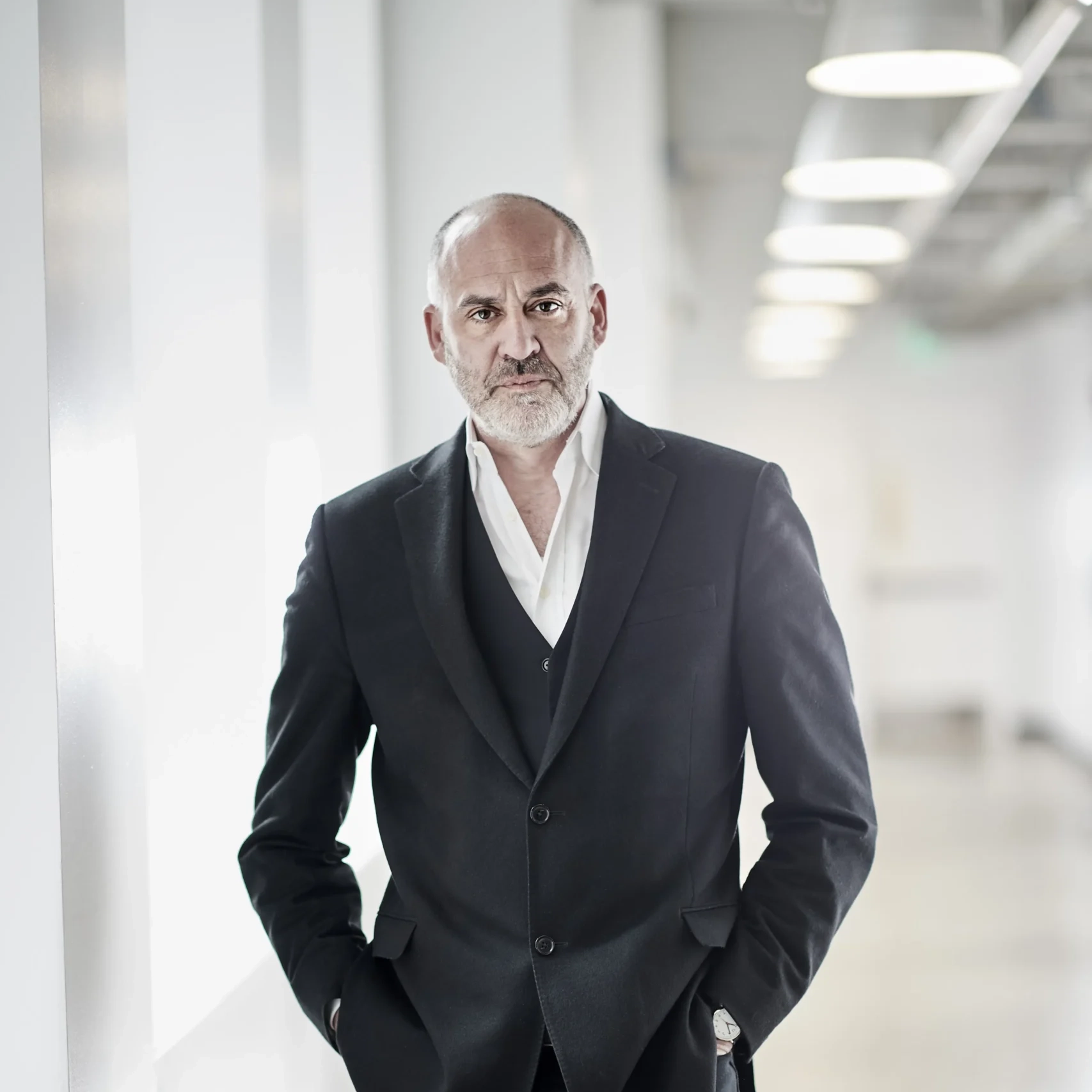 A headshot of Paul Snyder, a mature man where a black suit and white button up shirt standing in a white hallway.
