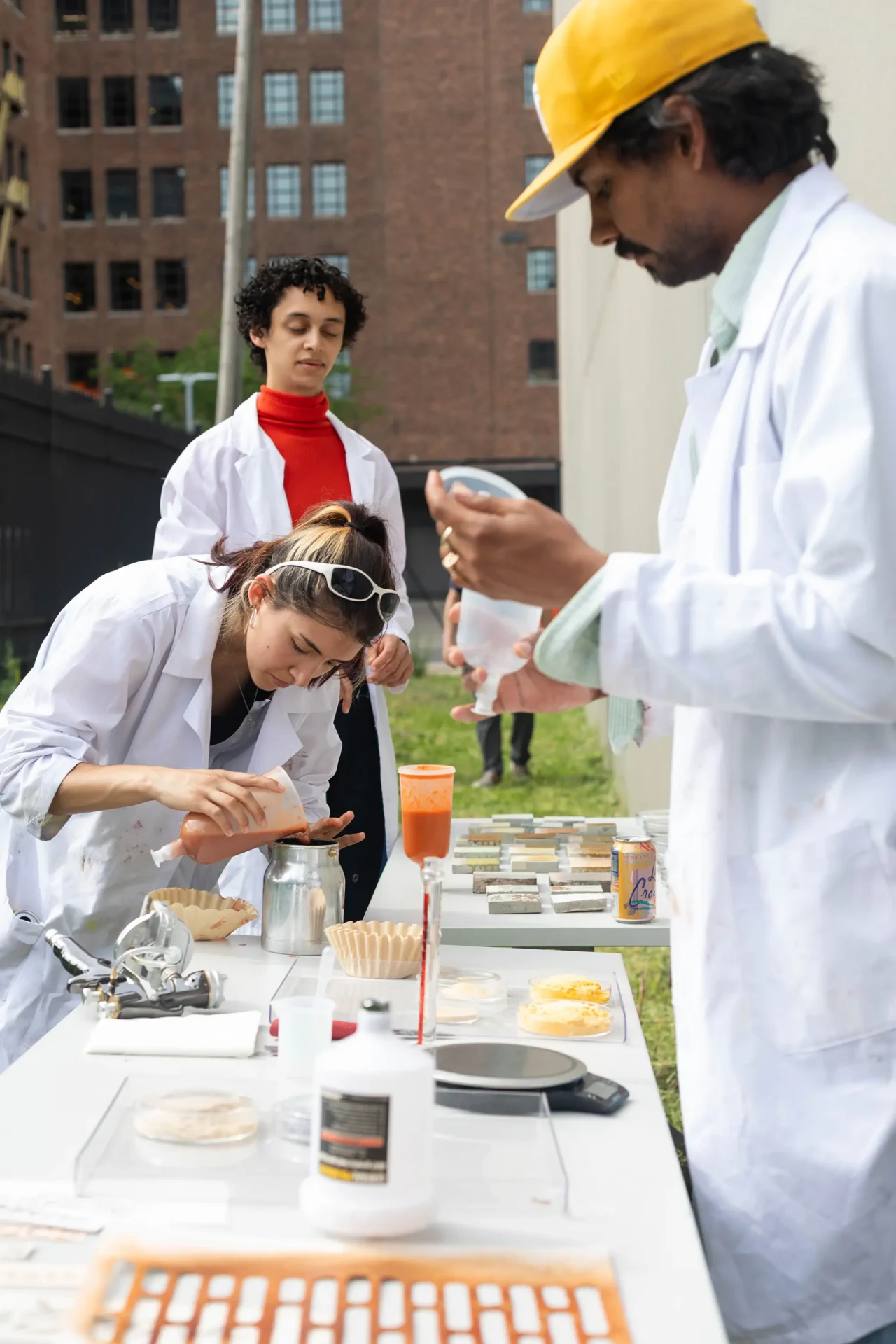 Three Color & Materials Design students wearing white lab coats demonstrating their method for creating sustainable spray paint from upscaling food waste streams