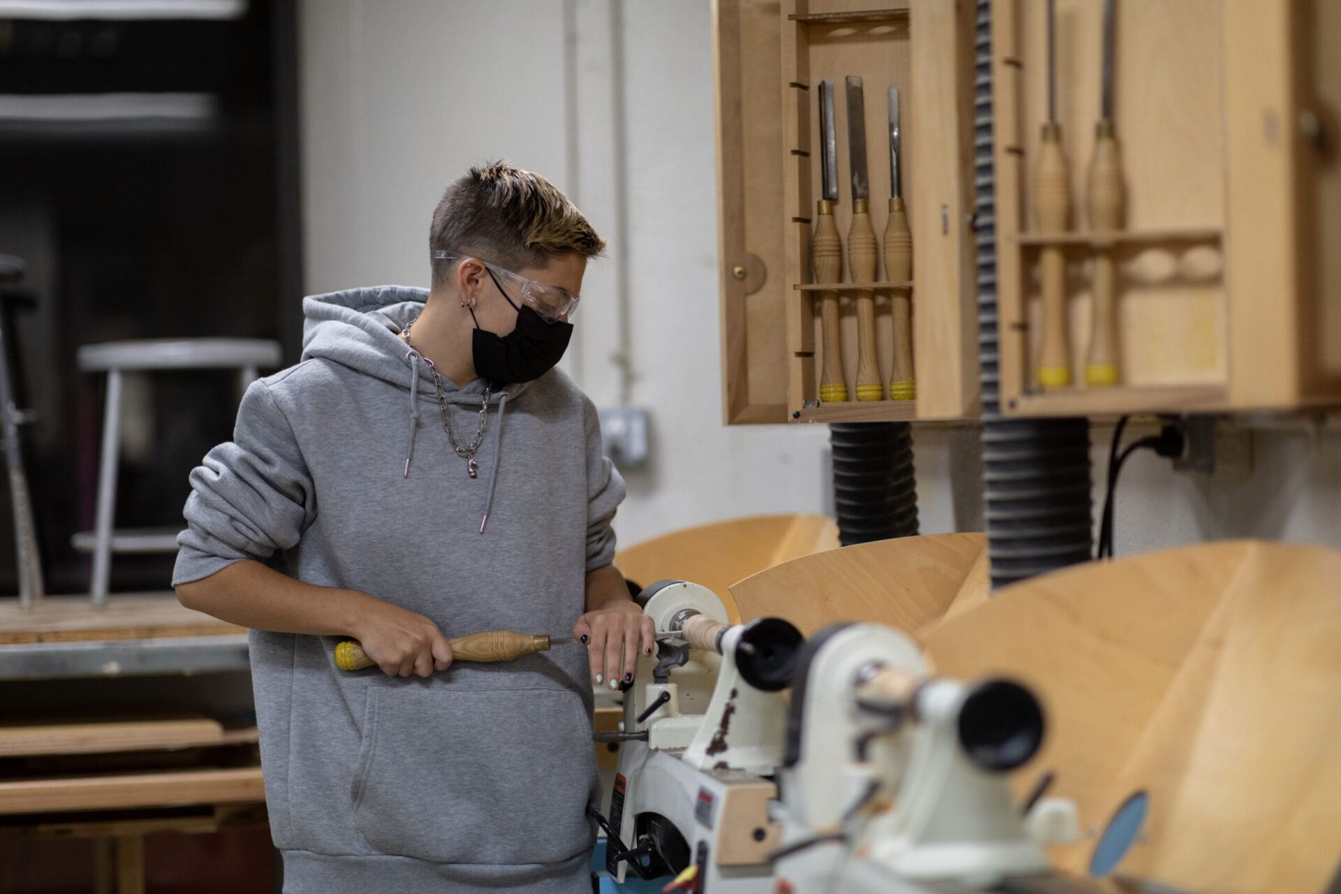 A student working on lathe. They are wearing a mask and goggles