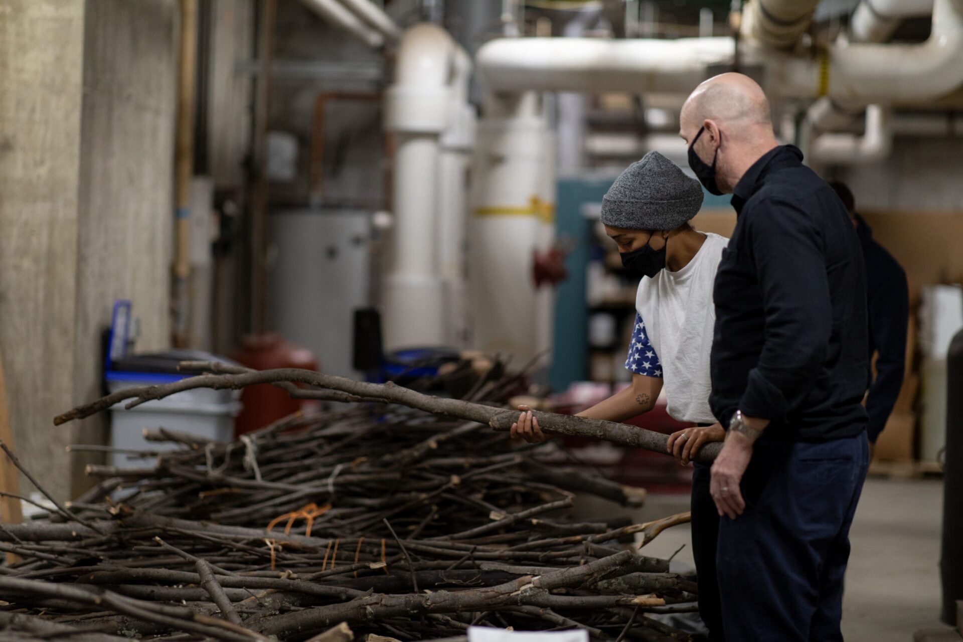 A student and teacher examining a pile of large branches. The student is holding one in her hands