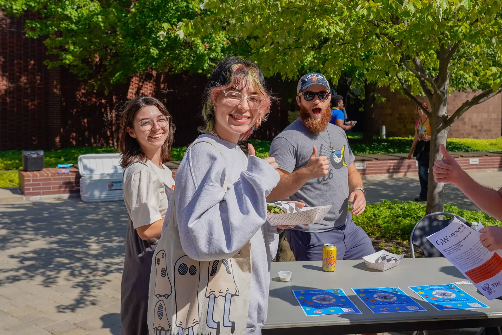 Three students smiling and giving thumbs ups for a photo outside