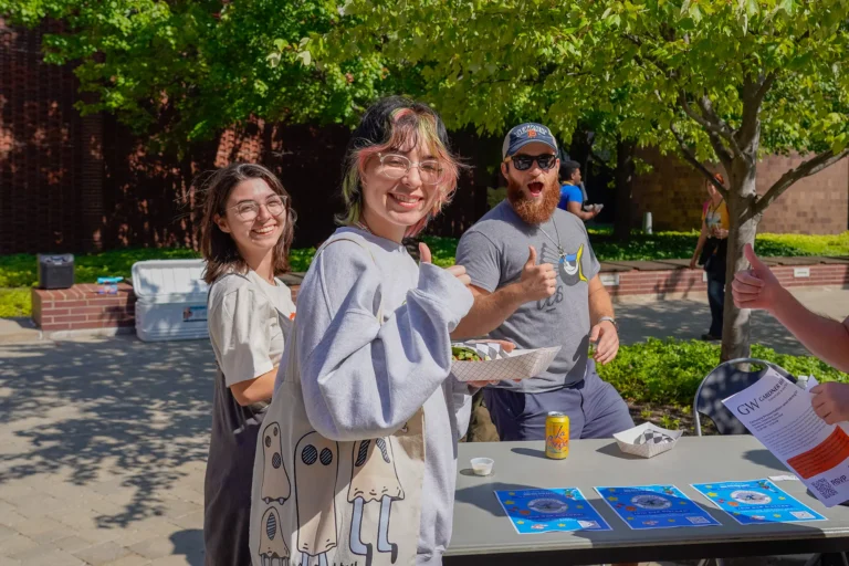 Three students smiling and giving thumbs ups for a photo outside