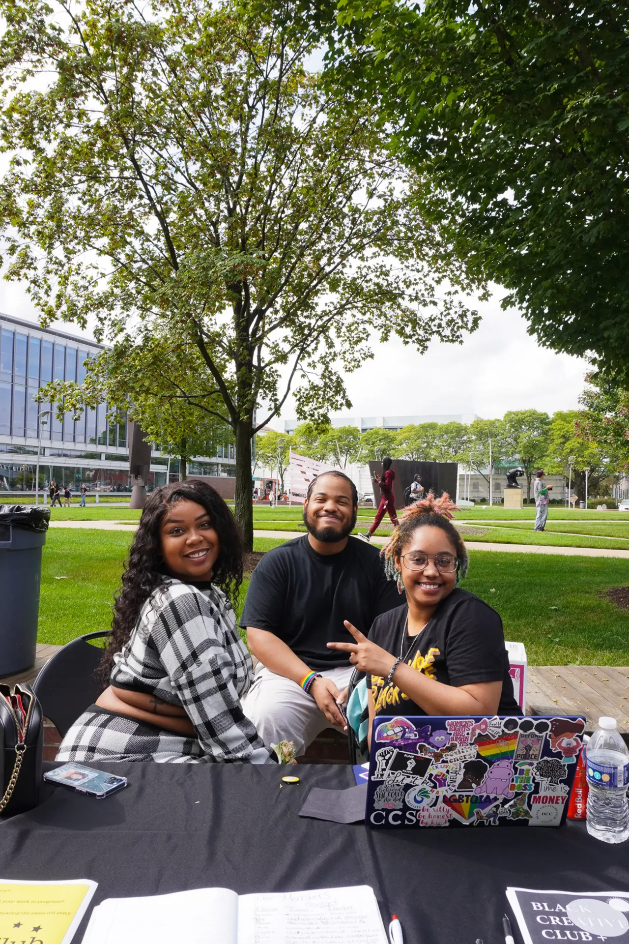Three students smiling, posing for a picture outdoors in front of a sculpture garden on the Ford Campus
