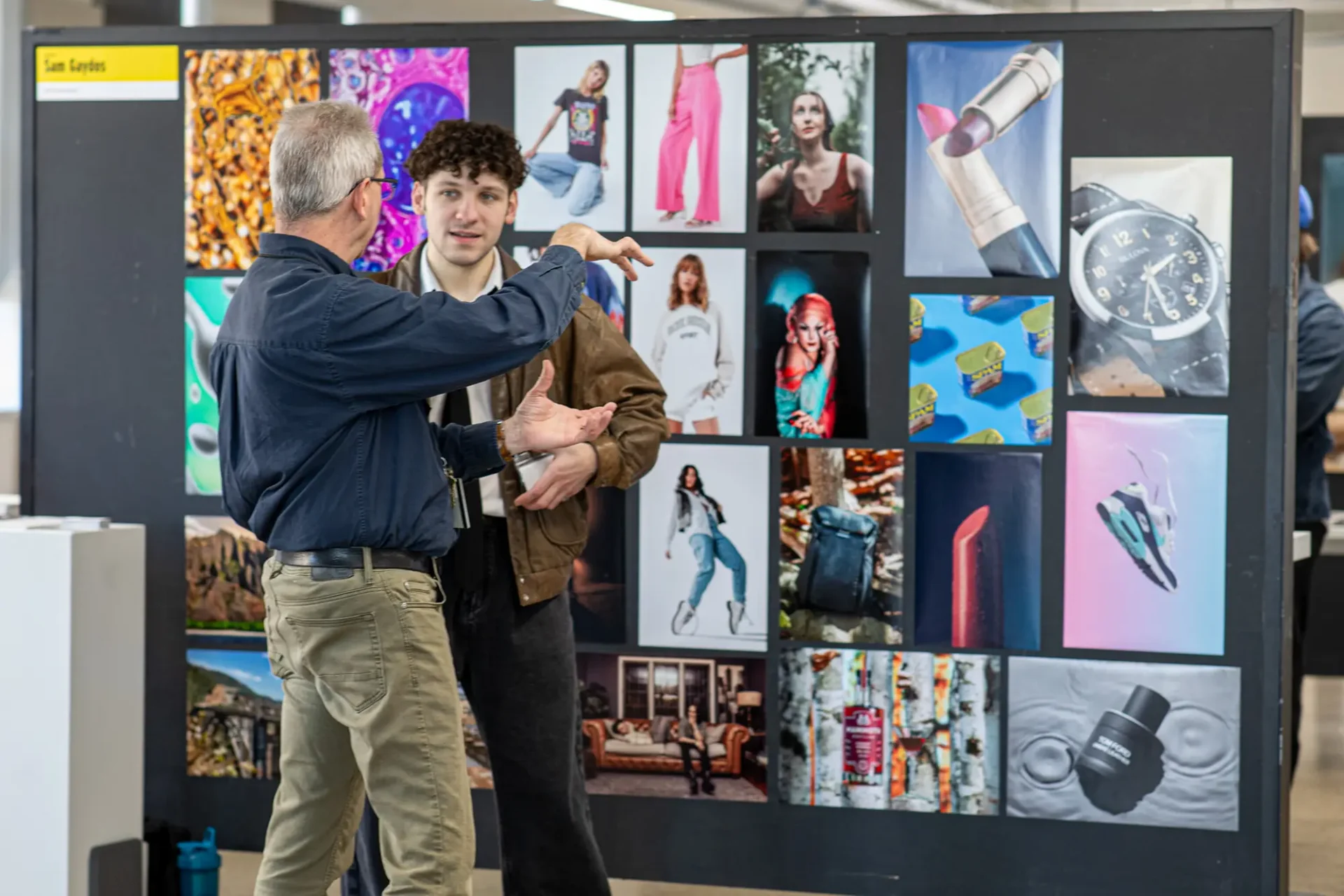 A student talking to a professor in surrounded by artwork boards