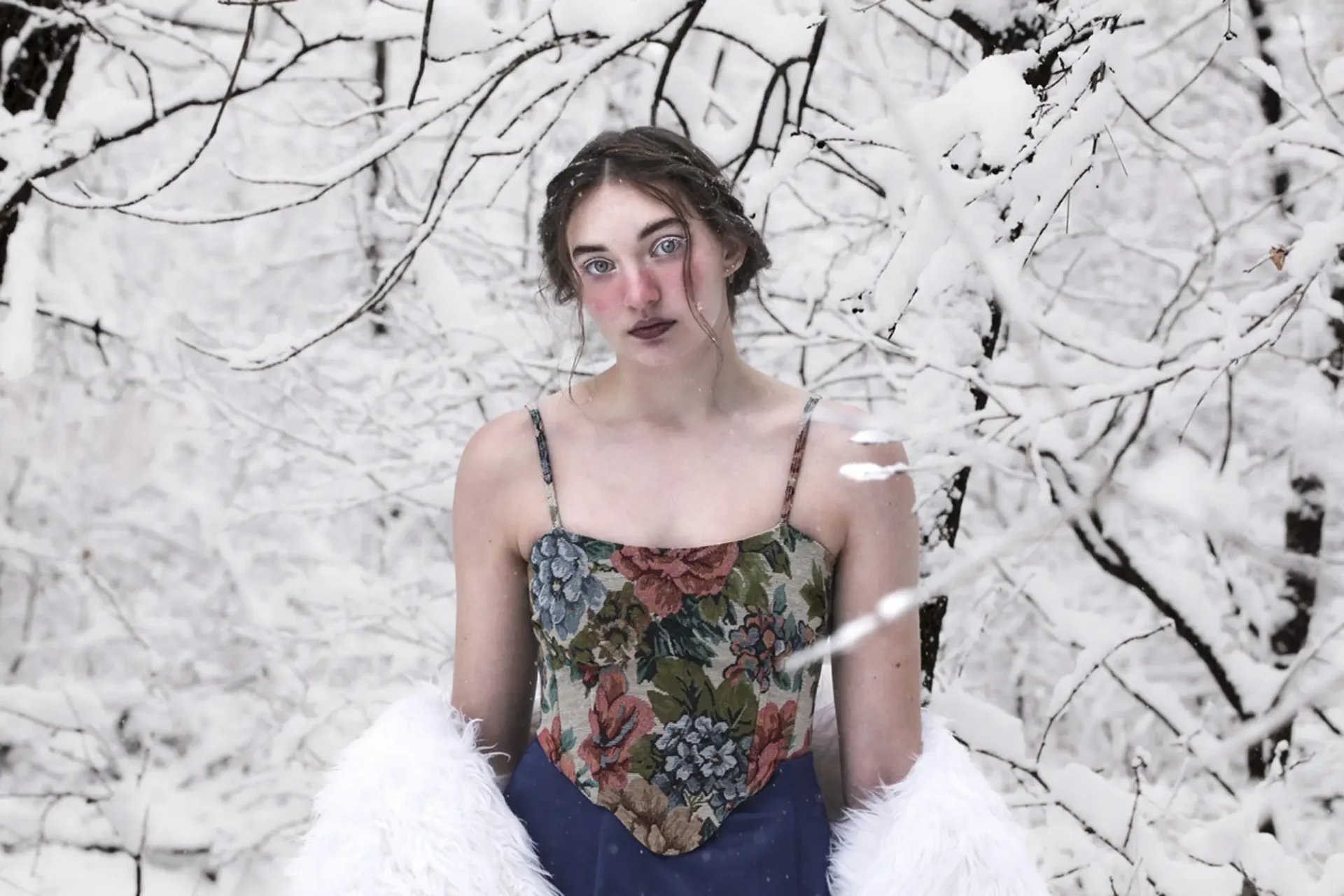 A photograph of a young girl in a dress surrounded by trees covered in snow