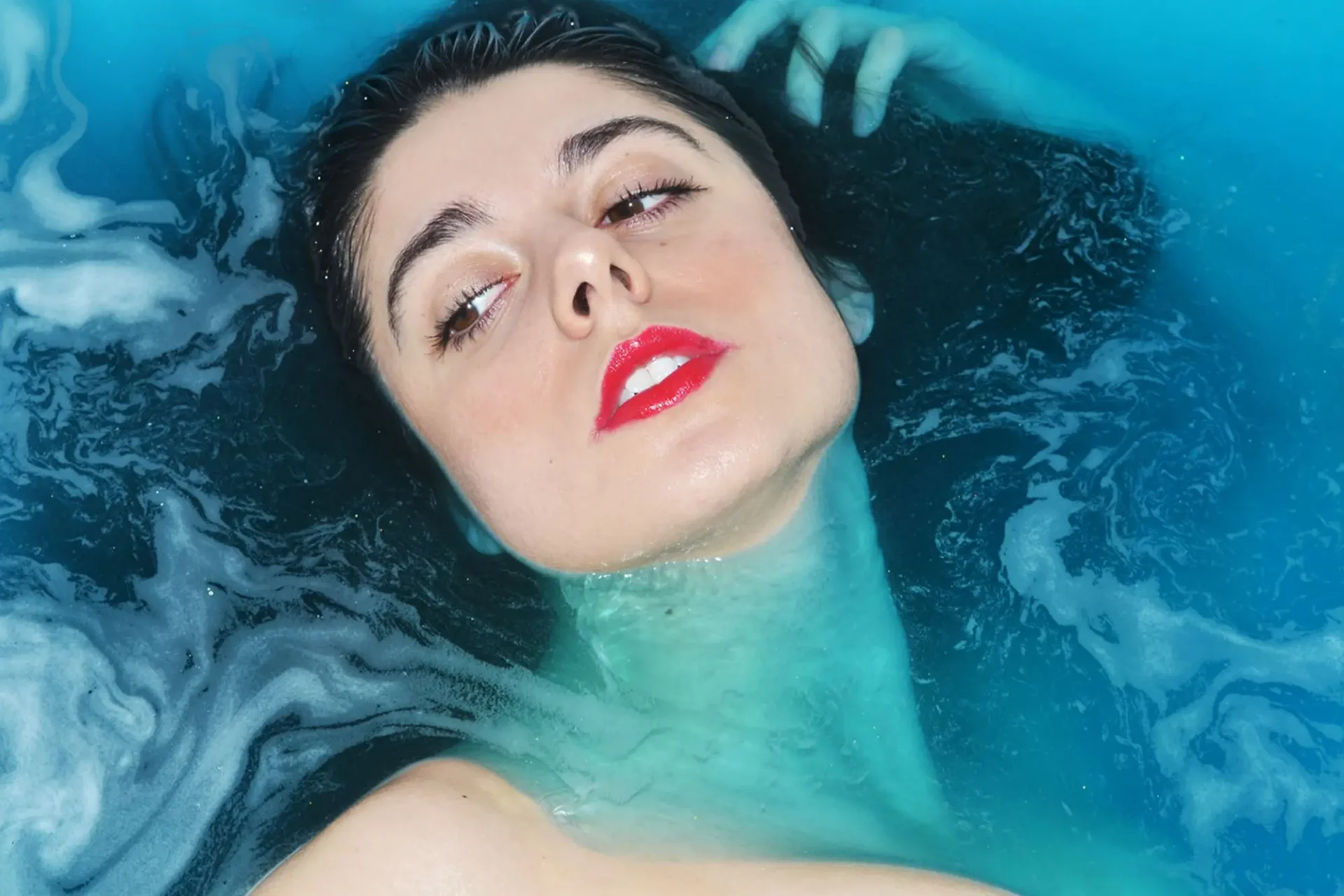 A photo of a woman's face emerging from deep blue water.