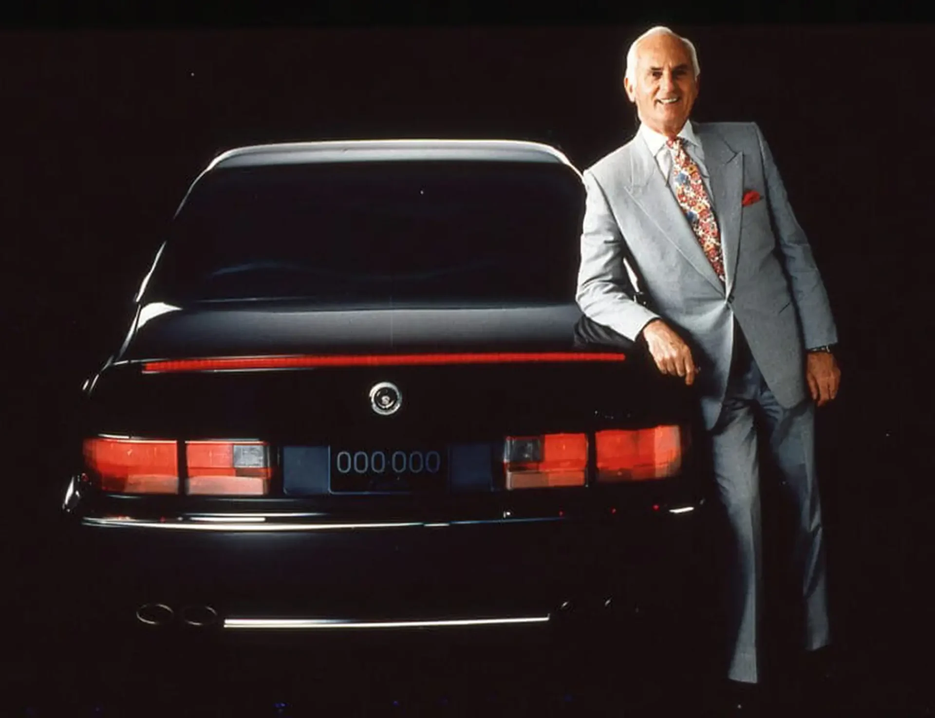 Chuck Jordan leaning against the back of a dark sedan, posing for a picture