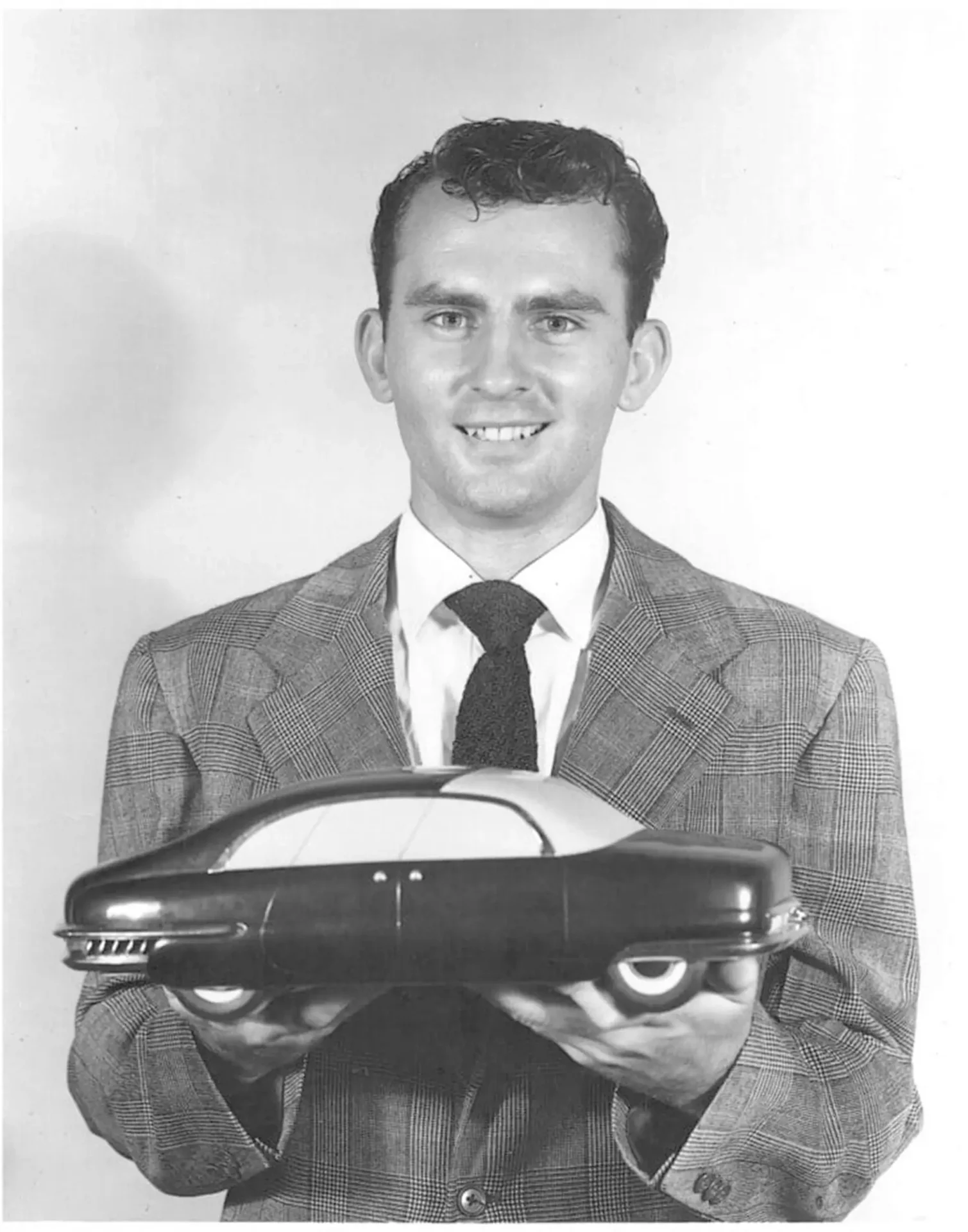 Chuck Jordan posing for a photo, holding up a small scale model of a car