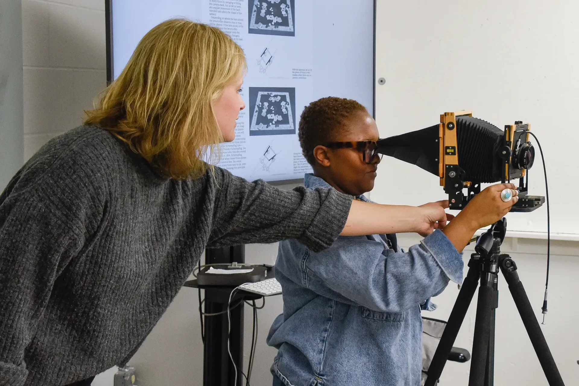 Faculty working with a student showing them how to use camera equipment.