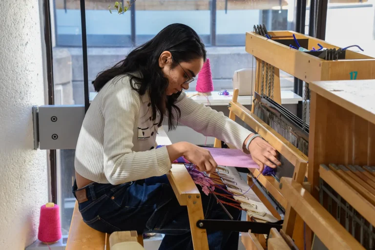 Fibers & Textile student weaving on a loom.