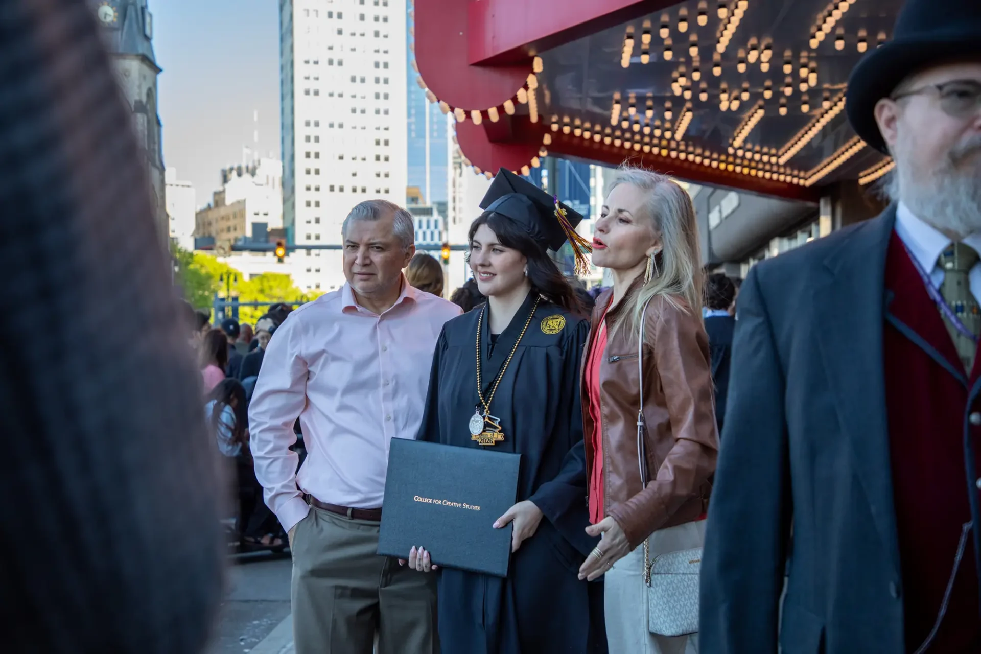A student posting with her parents in front of the venue holding her diploma