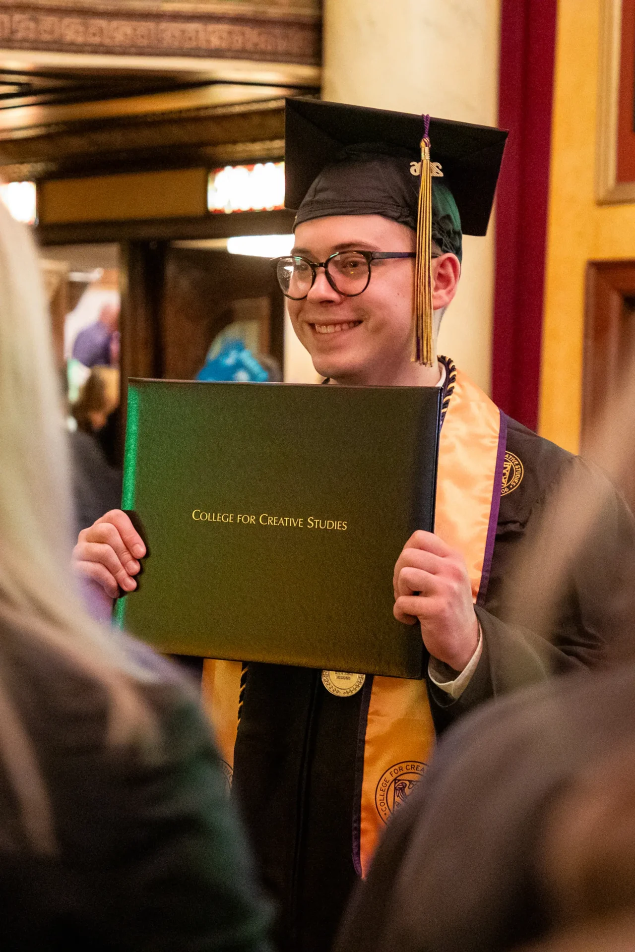 A student smiling, holding up their diploma