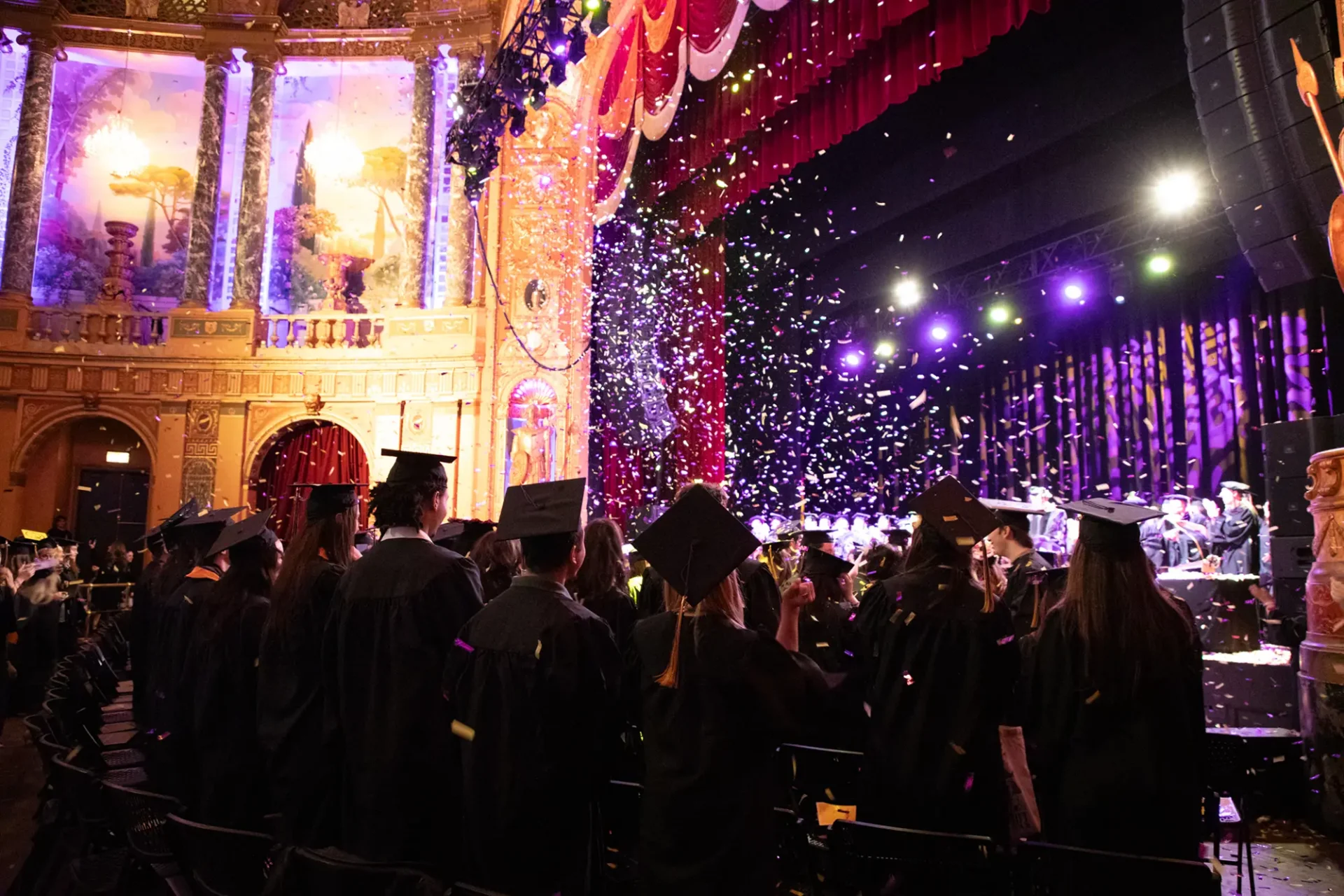 Graduates look at the stage as brightly colored confetti drops from the ceiling