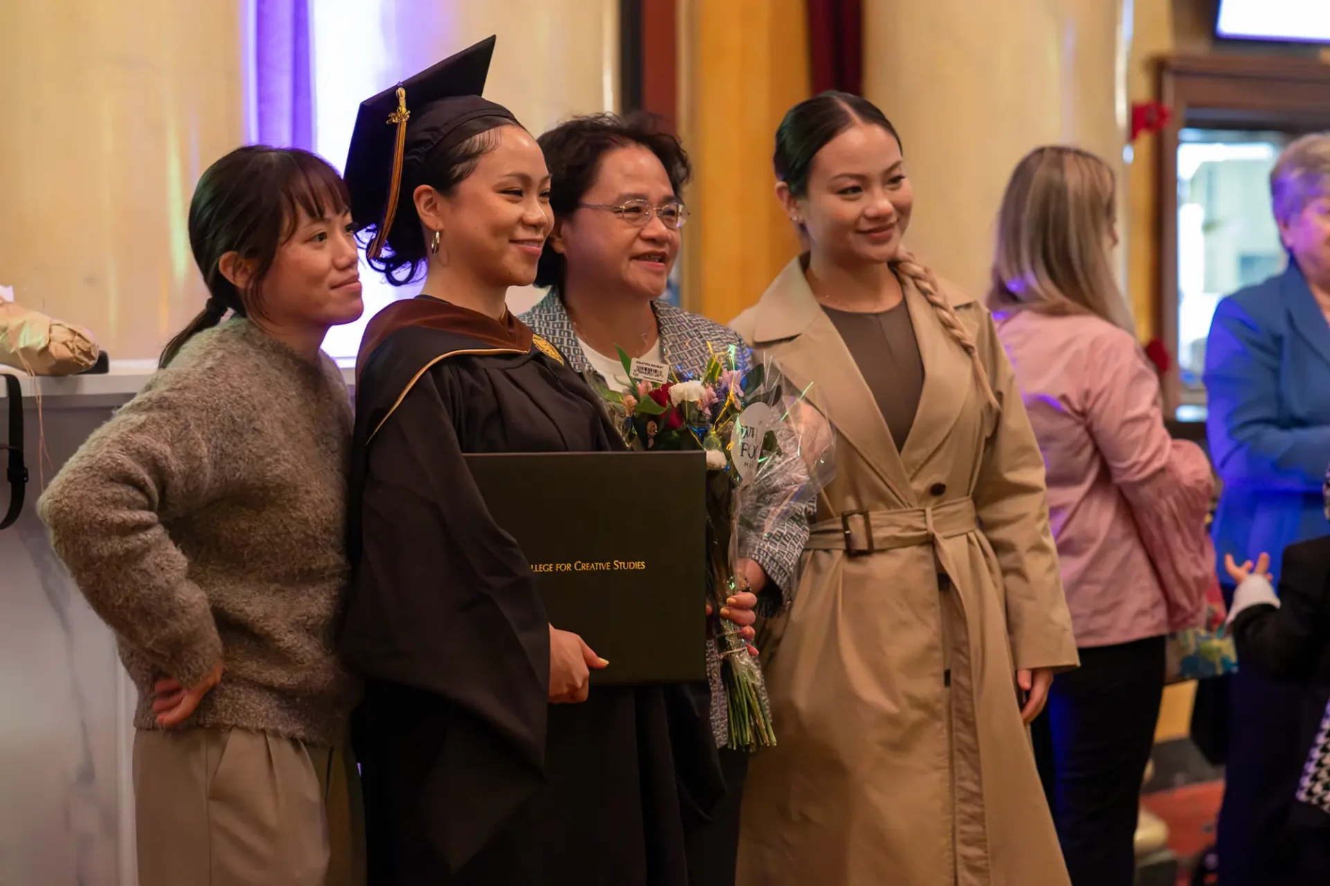 A student smiles and poses, proudly, with her parents, holding her diploma and flowers