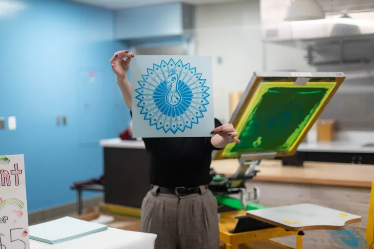 Alumni holding up a screen print of a peacock with "CCS" in it.