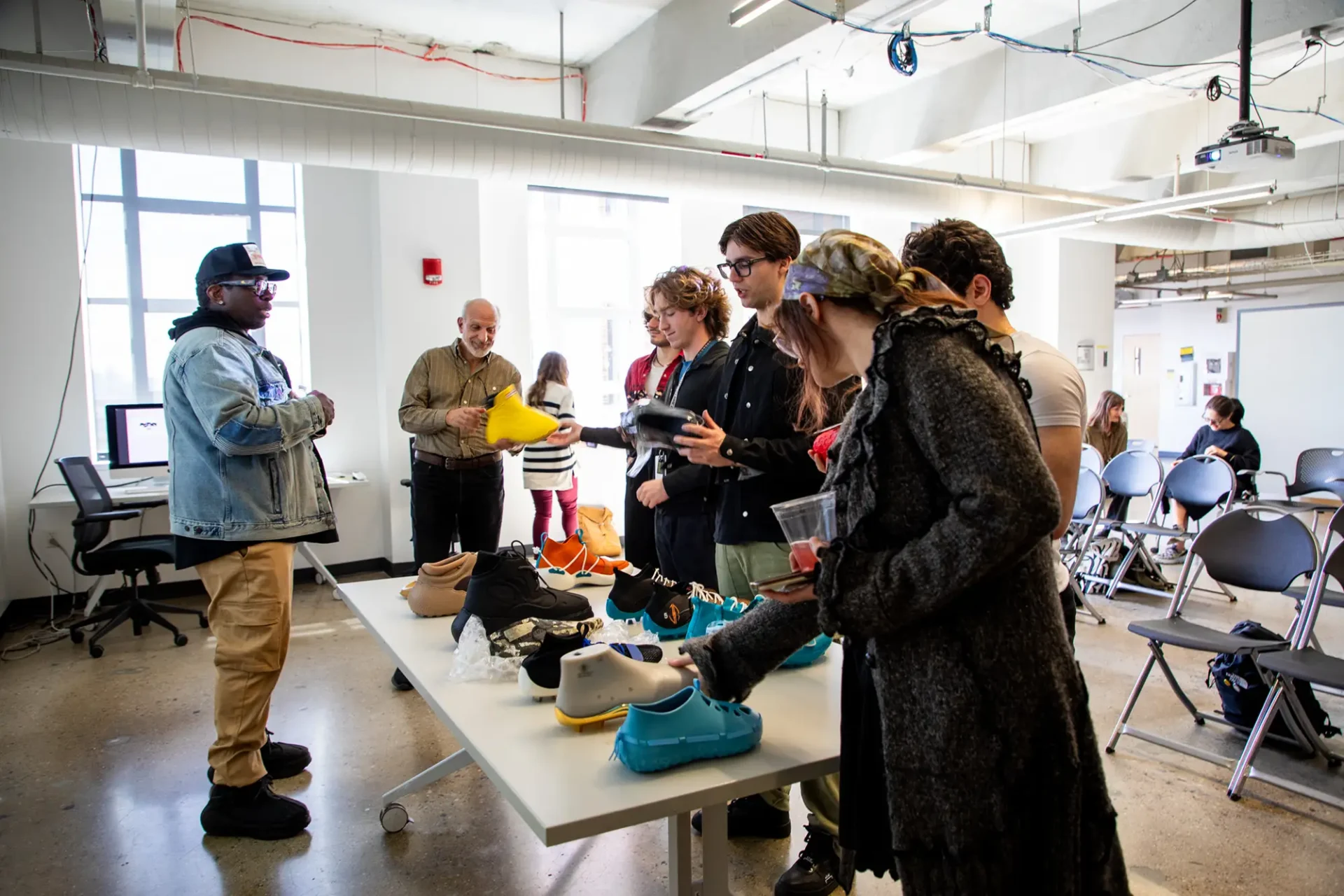 A group of students admiring and talking about different shoe designs and molds at a table in a classroom