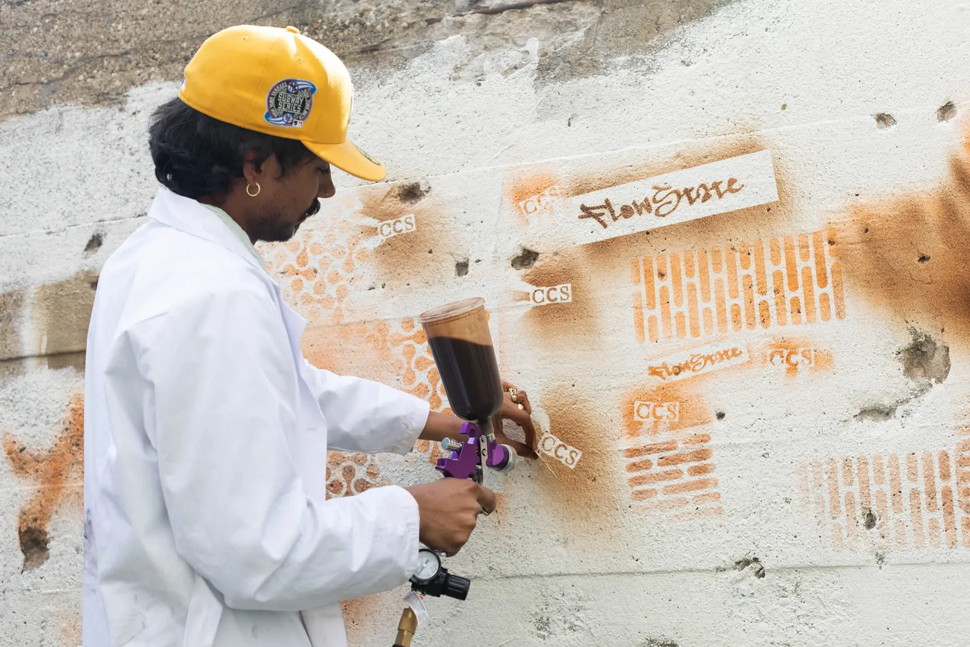 A Color & Materials Design student wearing a white lab coat demonstrating the application of their sustainable spray paint from upscaling food waste streams