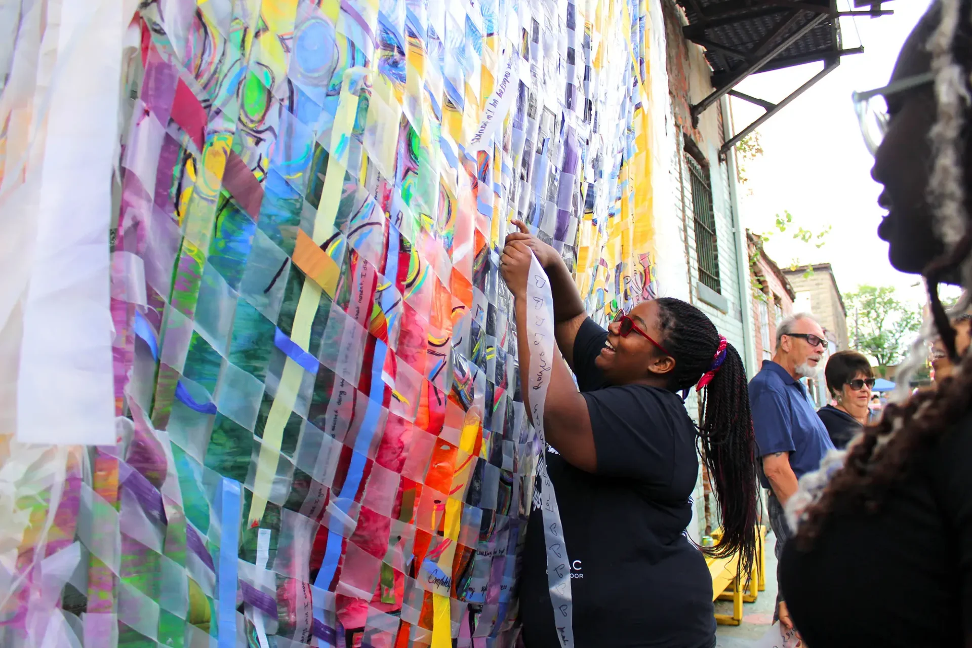 Someone working on a woven fabric as part of a mural in the city.