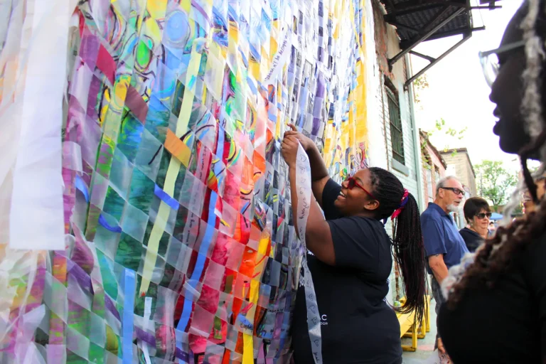 Someone working on a woven fabric as part of a mural in the city.