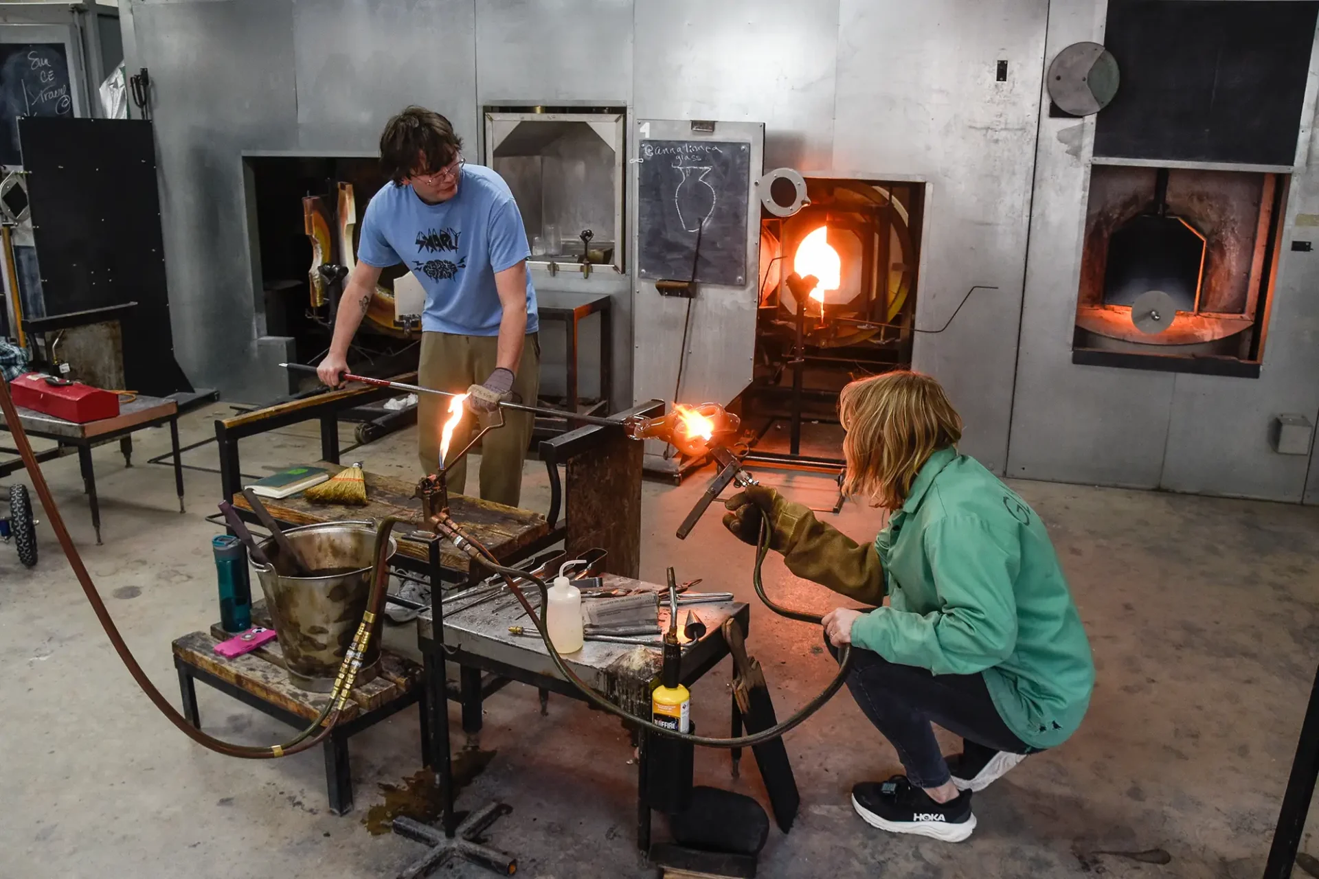 Faculty working with a student in the glassblowing studio.