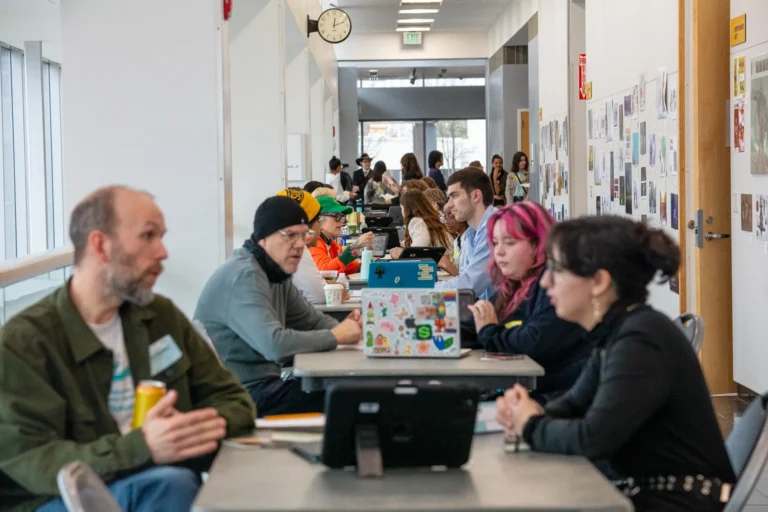 Faculty and industry professionals discussing portfolio work with students in a long hallway