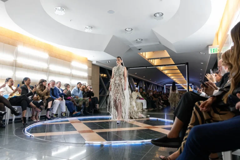 A fashion model walking down a catwalk surrounded by people taking photos