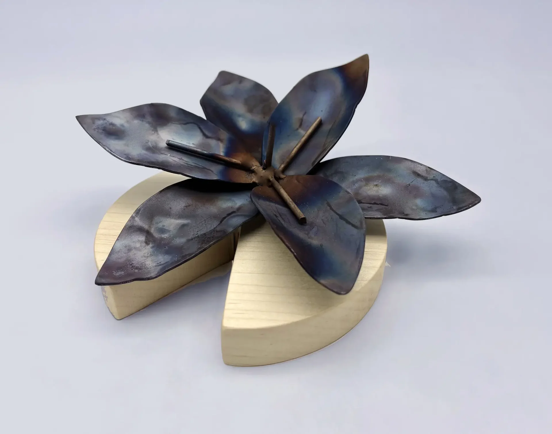 3D sculpture of a metal flower on a round wood base.