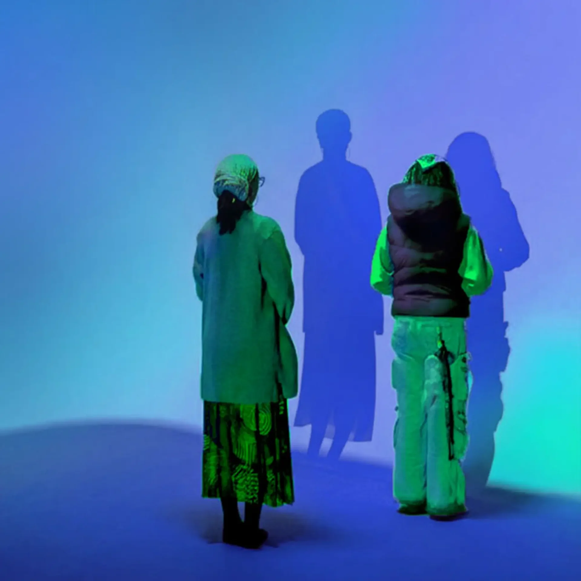 Photograph of two women staring at their shadows against a blue wall.