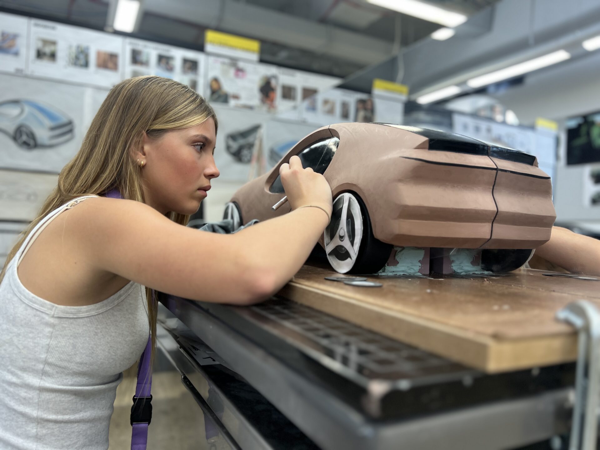 A design student meticulously applying detail to a clay scale model of a sports car in an automotive studio.