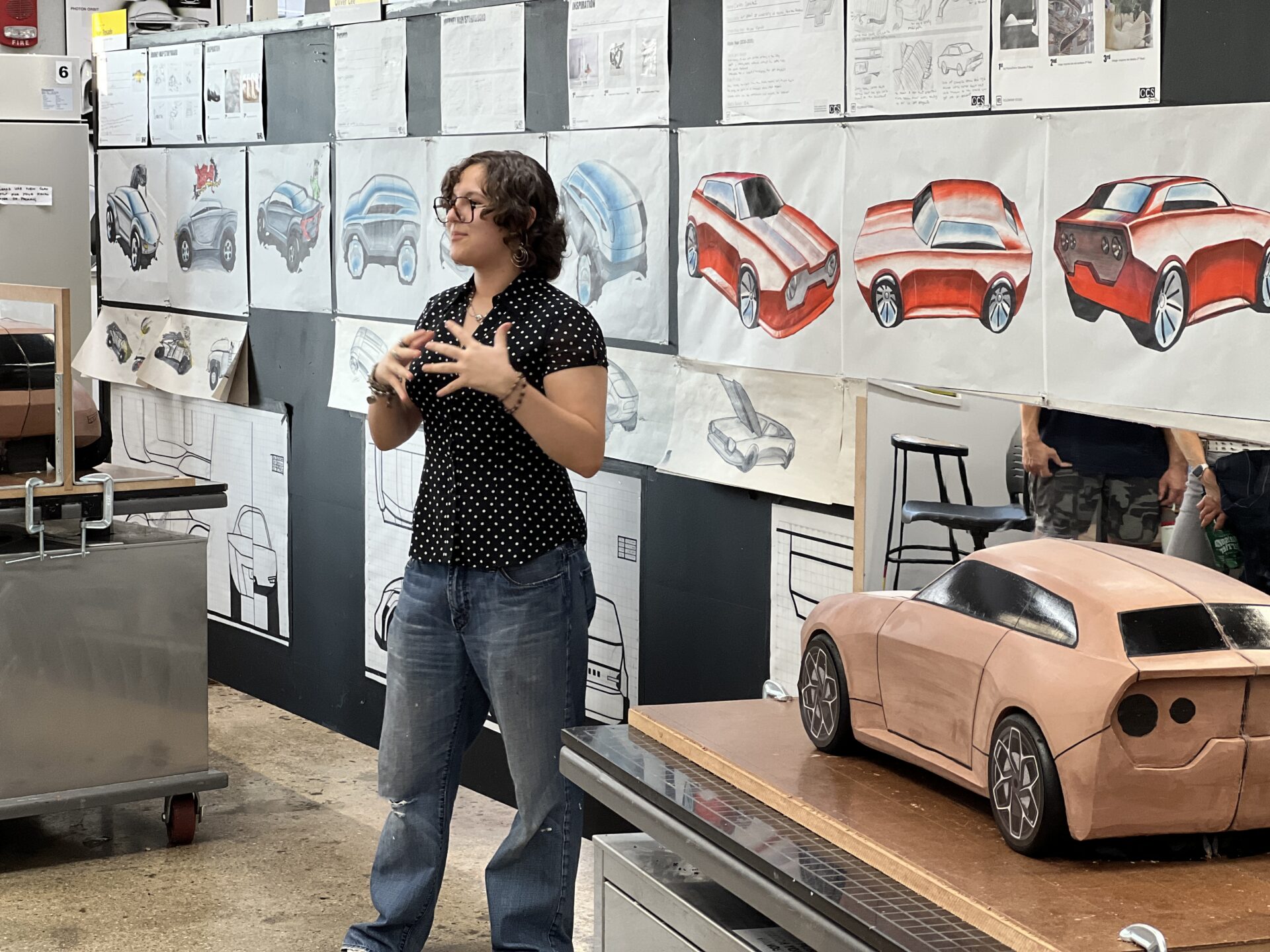 A student presenting a car design project with sketches and a clay model.