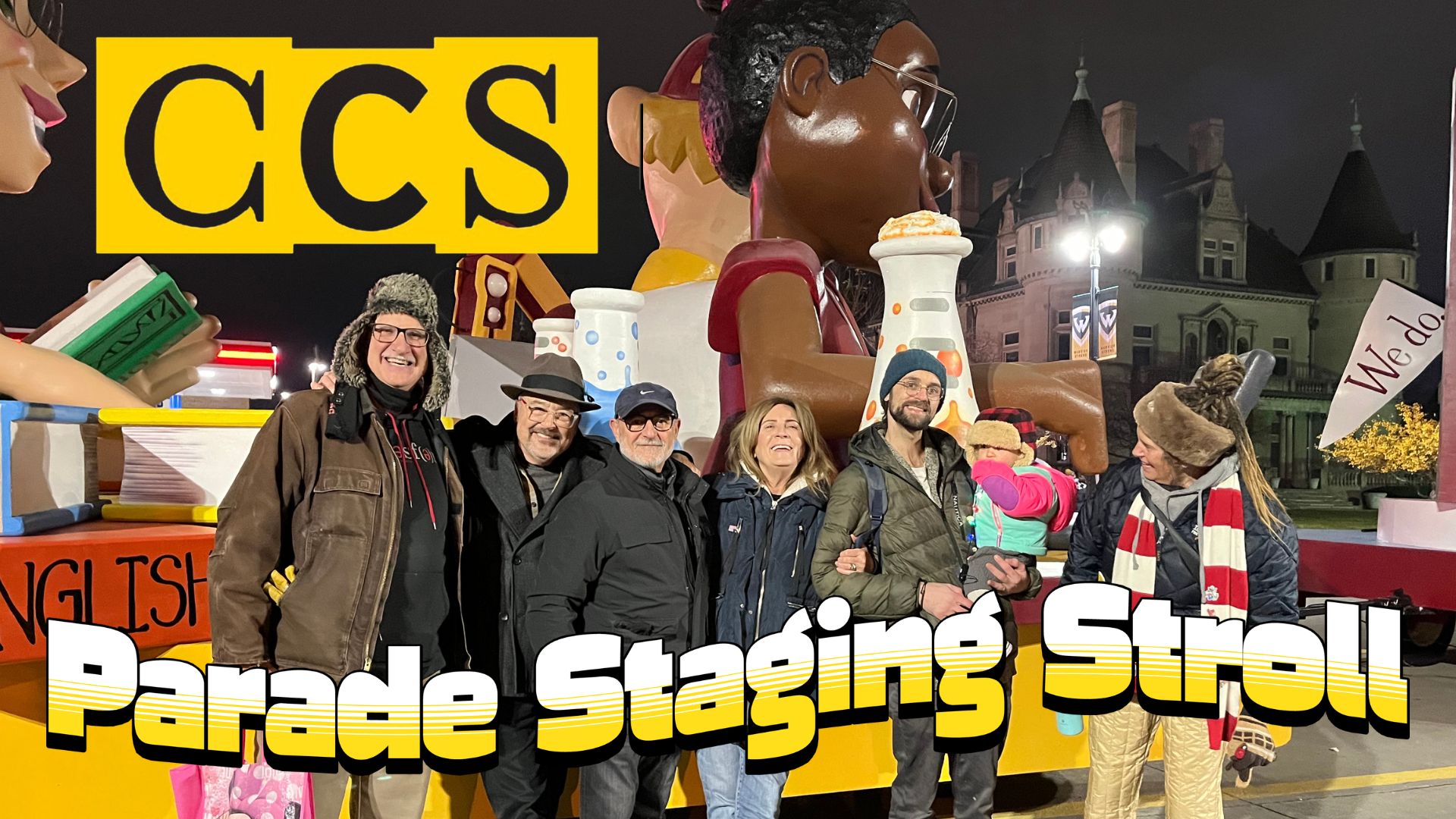 A group of people dressed in winter gear posing together in front of a colorful parade float at night, with text overlay reading "����ר�� Parade Staging Stroll."