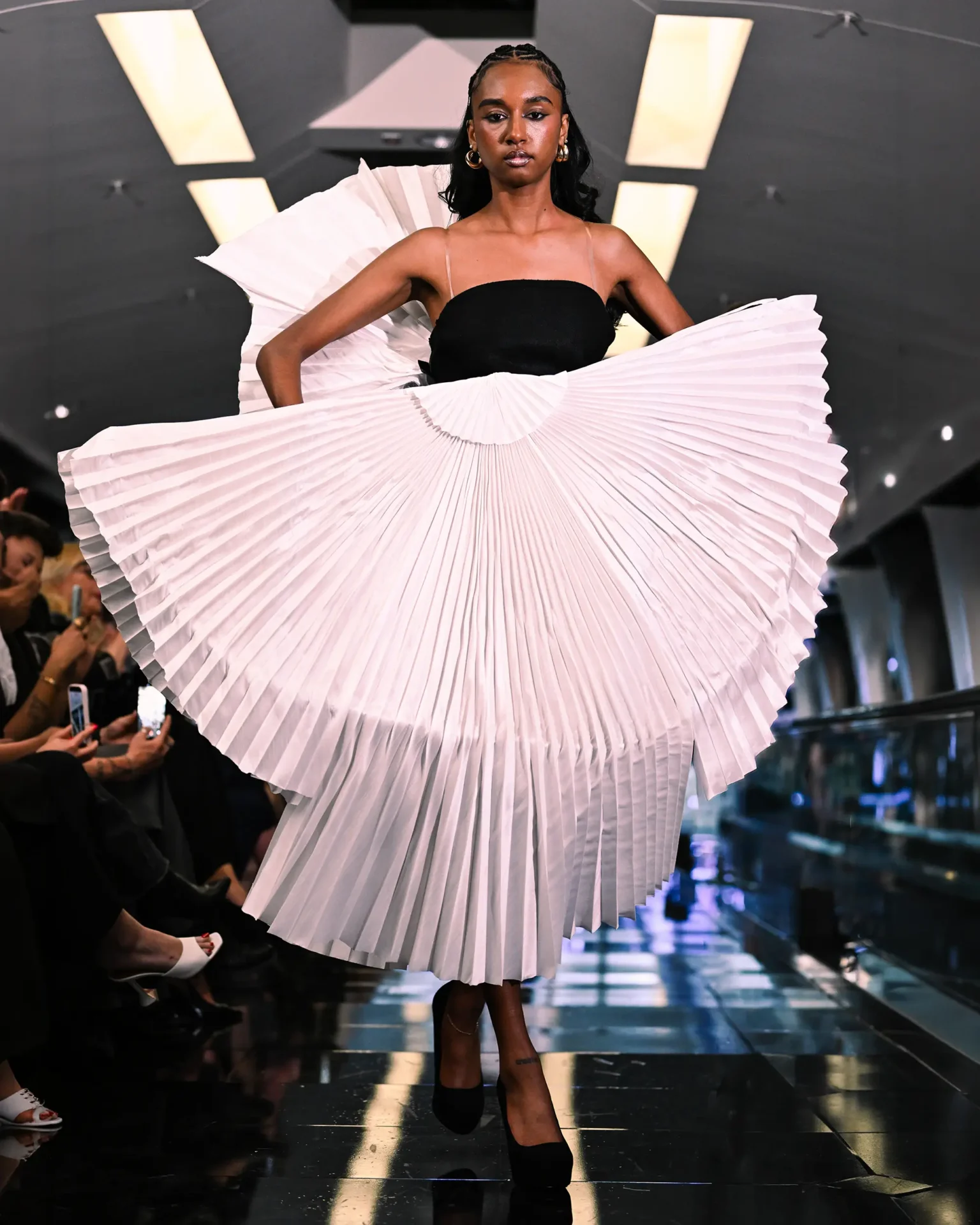 Model walking the runway wearing a black topwith large white pleated skirt.
