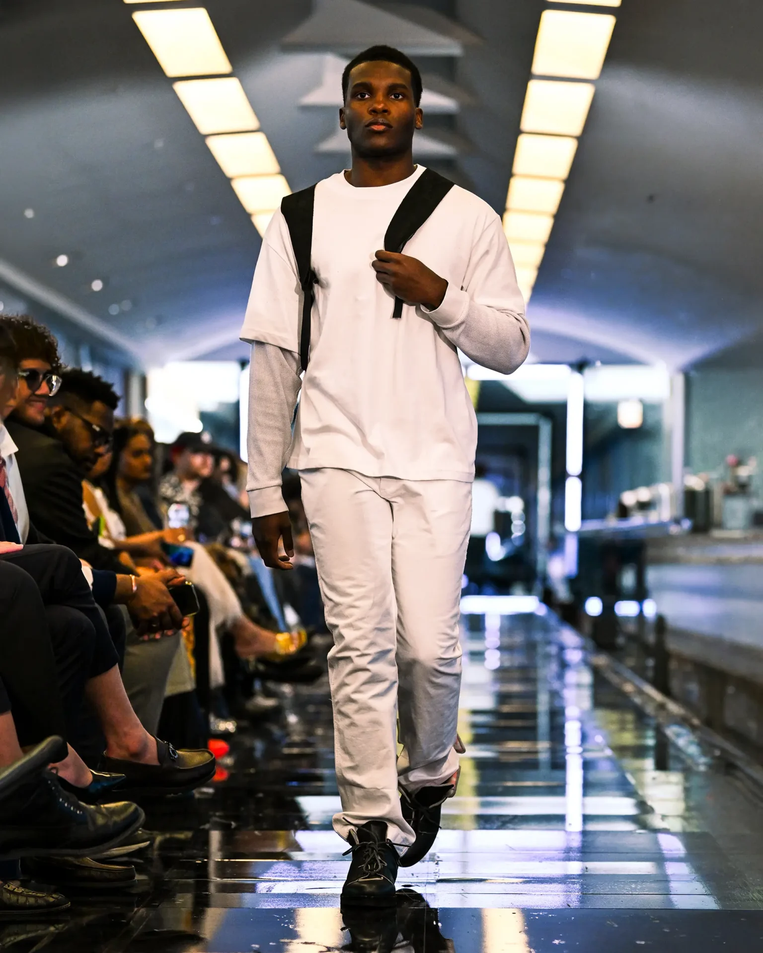 Model walking the runway wearing a white layered outfit with black straps and black shoes.