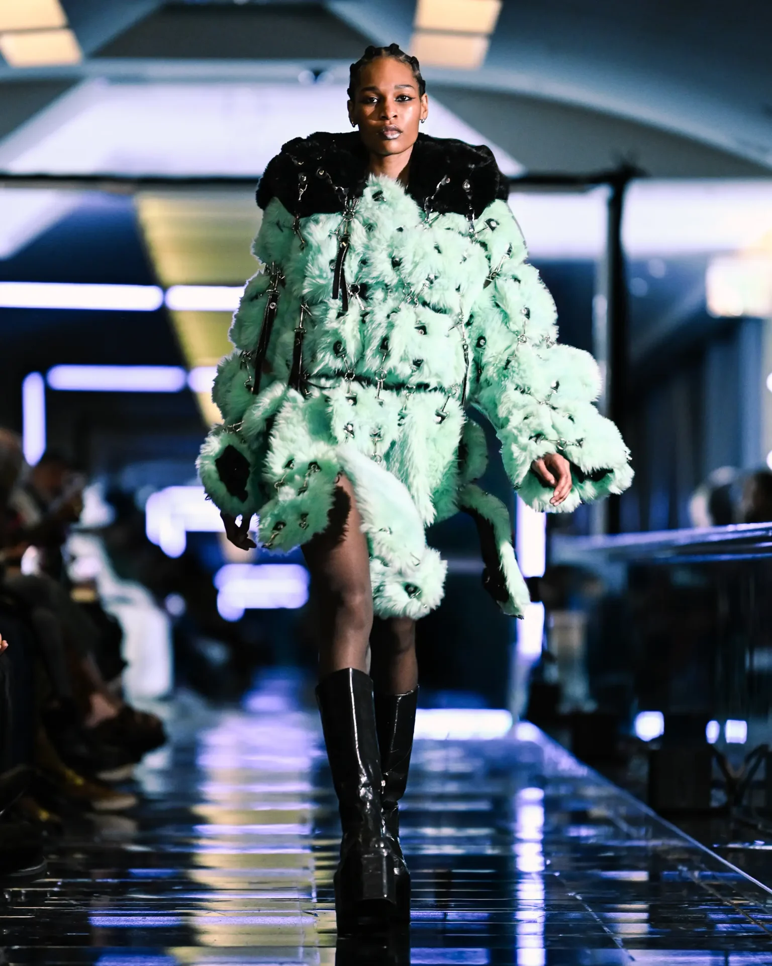 Model walking the runway wearing a mint green textured coat and black platform boots.