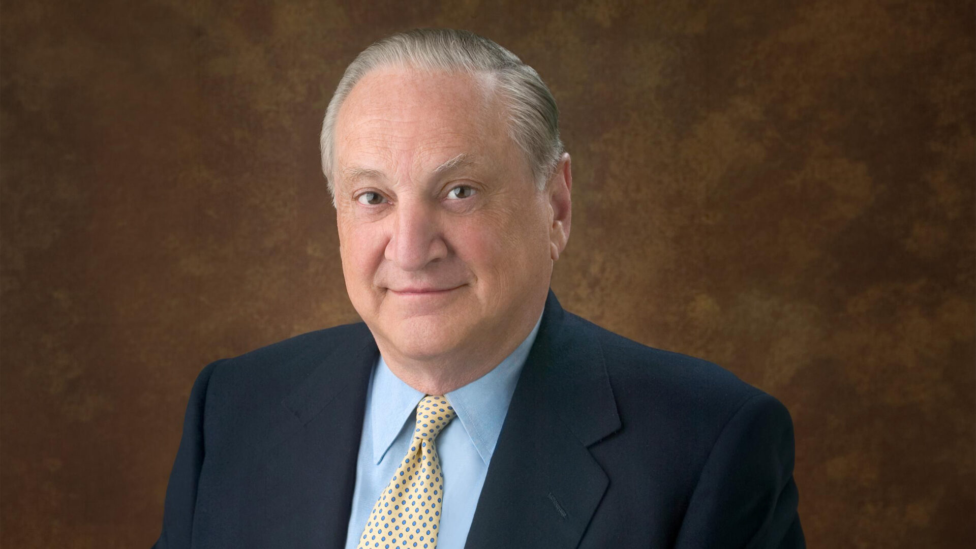 Headshot of Richard Manoogian in a dark suit, light blue shirt, and patterned gold tie.