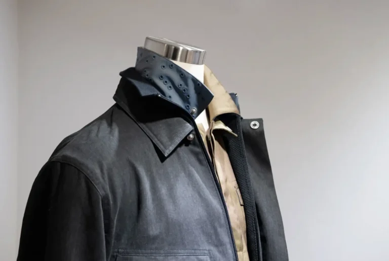 A mannequin displaying layered clothing, including a dark jacket, a brown collared shirt, and a dark blue inner collar detailed with rows of metal eyelets.